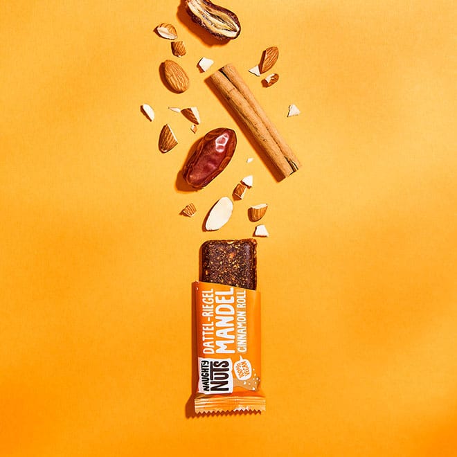 Bio Dattel-Riegel Mandel Cinnamon Roll mit Datteln, Mandeln und Zimtstangen auf orangefarbenem Hintergrund